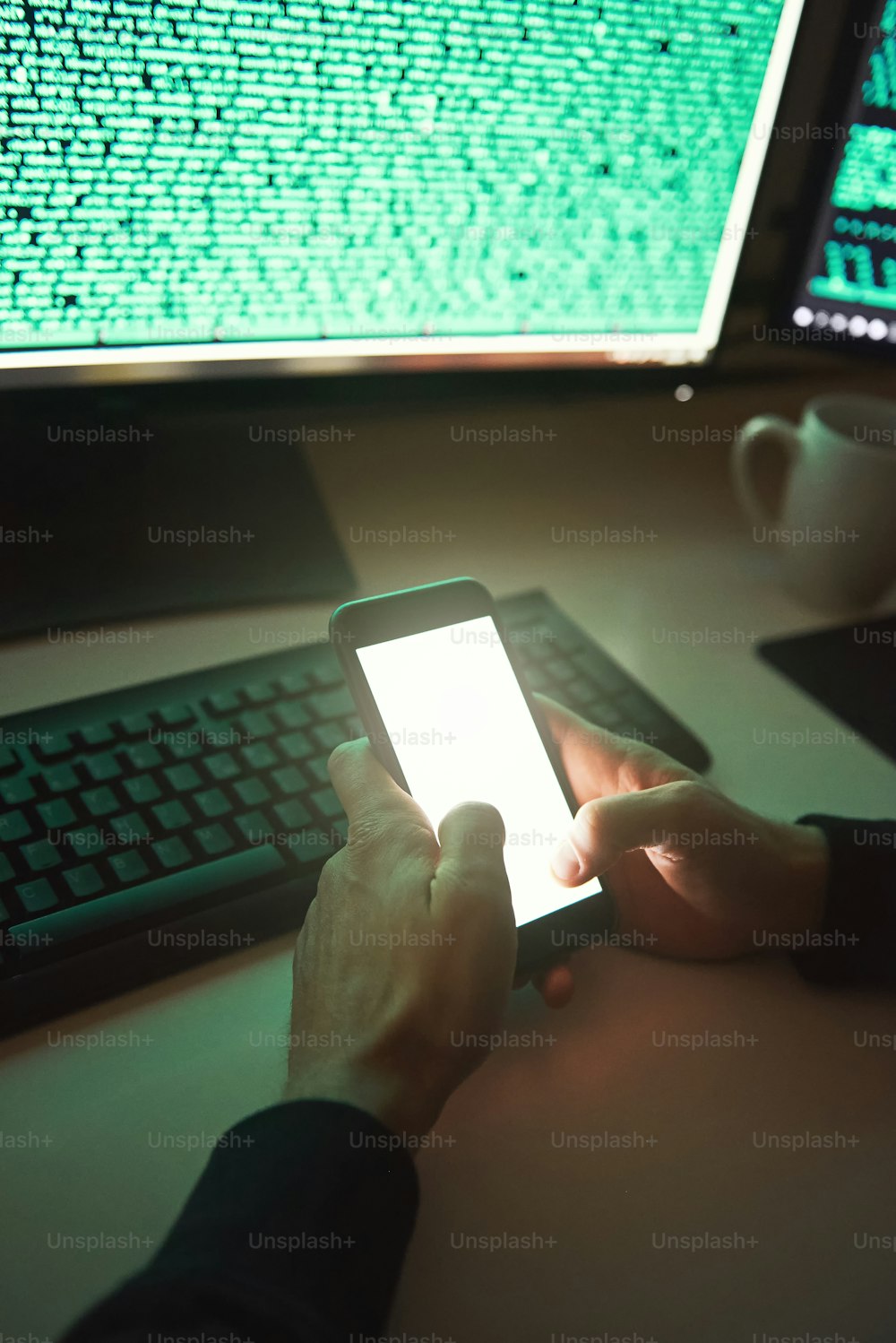 Professioneller Hacker. Nahaufnahme eines jungen Hackers in schwarzem Kapuzenpulli, der sein Smartphone benutzt, um Daten zu stehlen, während er in einem dunklen Raum sitzt. Binärcode. Cyberangriff. Cybersicherheit