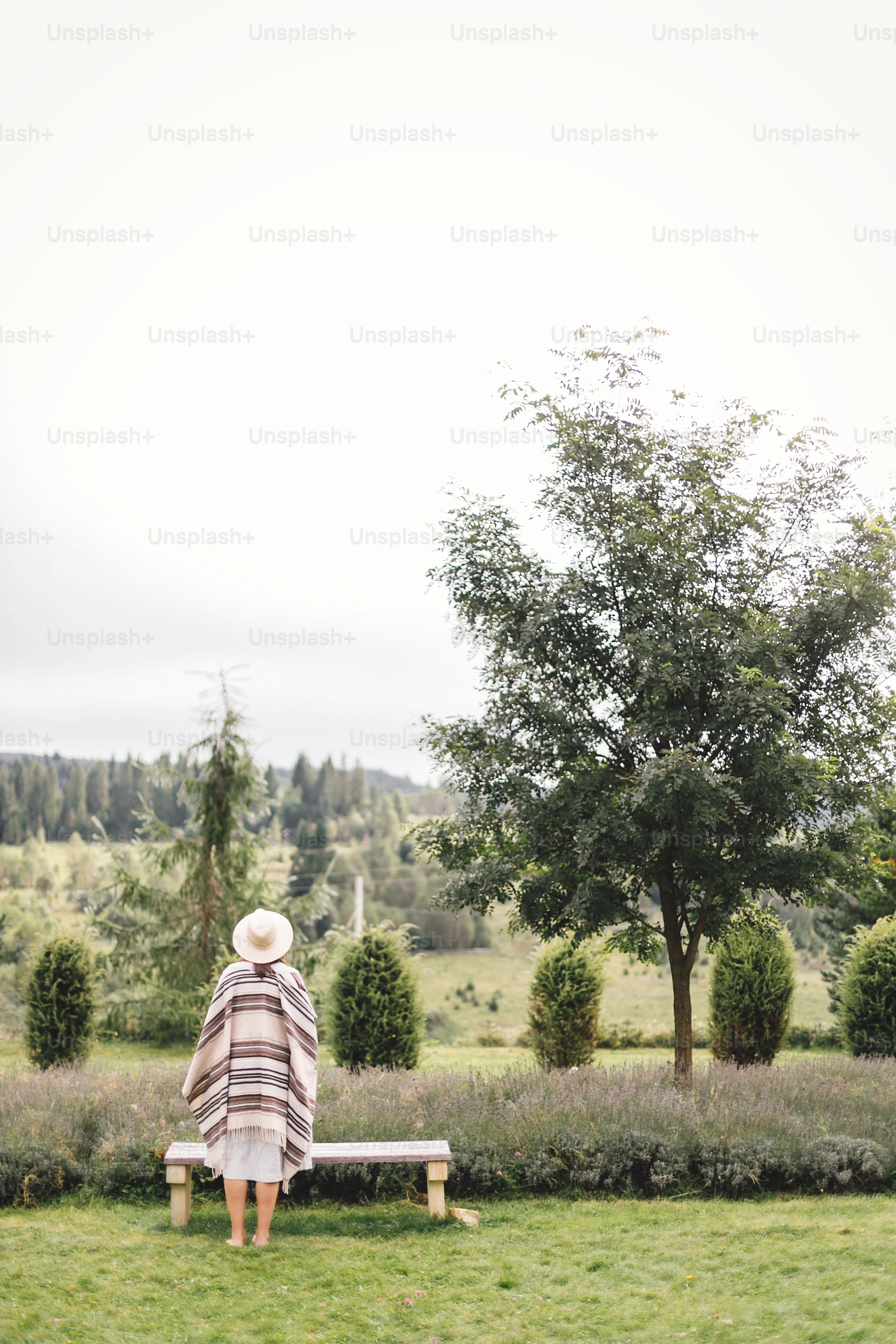Fille hipster élégante en poncho, robe en lin et chapeau posant au champ de lavande et se relaxant le matin. Femme bohème profitant de vacances à la montagne. Moment rustique atmosphérique. Espace de copie