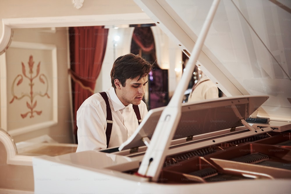 Beautiful man. Young professional musician in official clothes plays on the white piano.