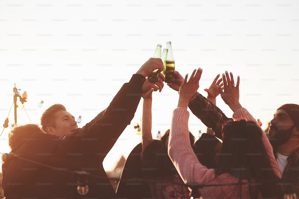 Bottles up. Holidays on the rooftop. Cheerful group of friends raised their hands up with alcohol.