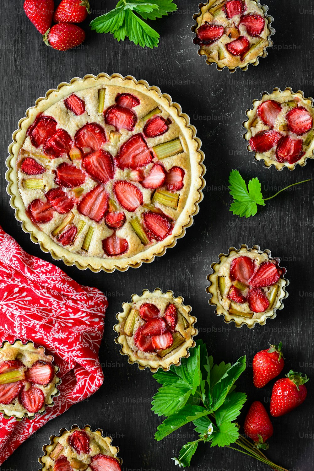 Homemade tarts with strawberry and rhubarb on black wooden background. Top view. Rustic style