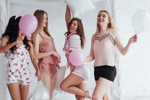Let's go crazy. Standing on the luxury white bad at holiday time with balloons and bunny ears. Four beautiful girls in night wear have party.
