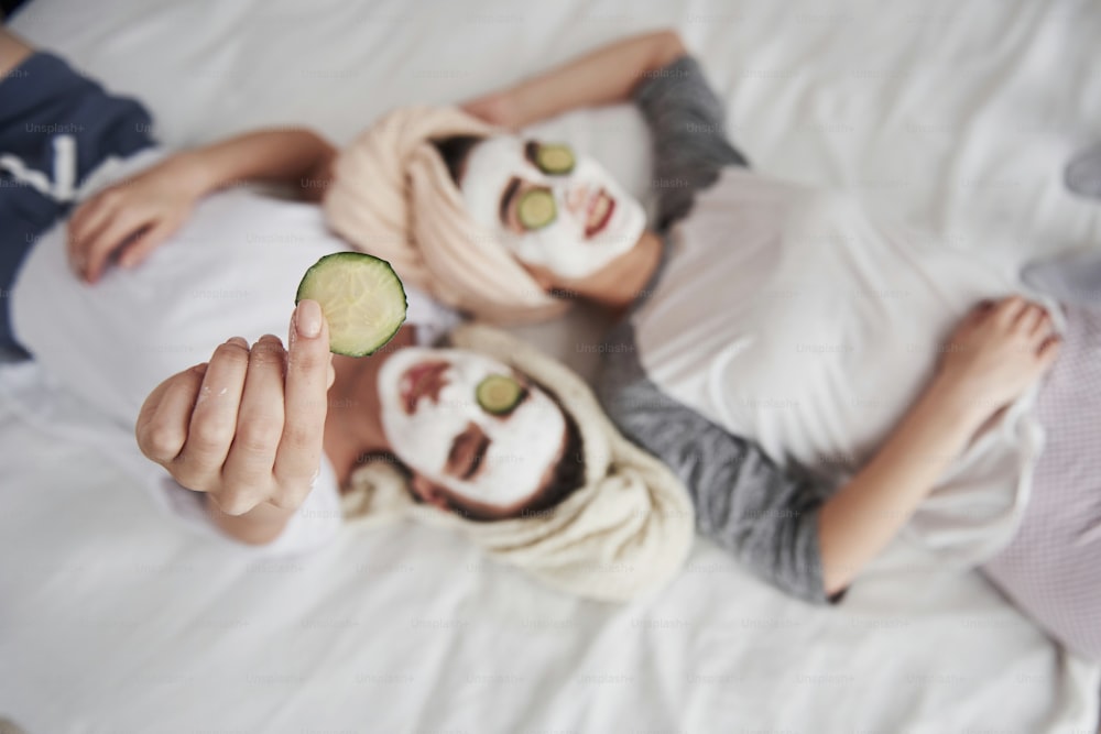 Conception of self care. Girl holds cucumber ring in the hand. Lying on the white bed. Top view.