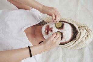 Top view of girl in white beauty mask on face and cucumber rings on eyes.
