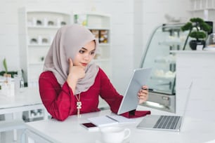 Young asian muslim woman is thinking and using a tablet in a white cafe