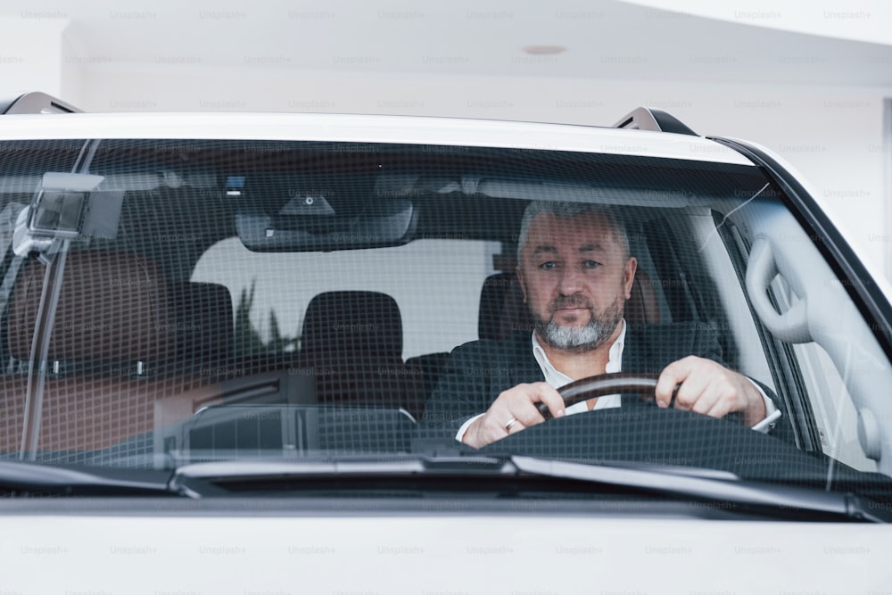 Look into the camera. Front view of senior businessman in his new modern car testing new functions.