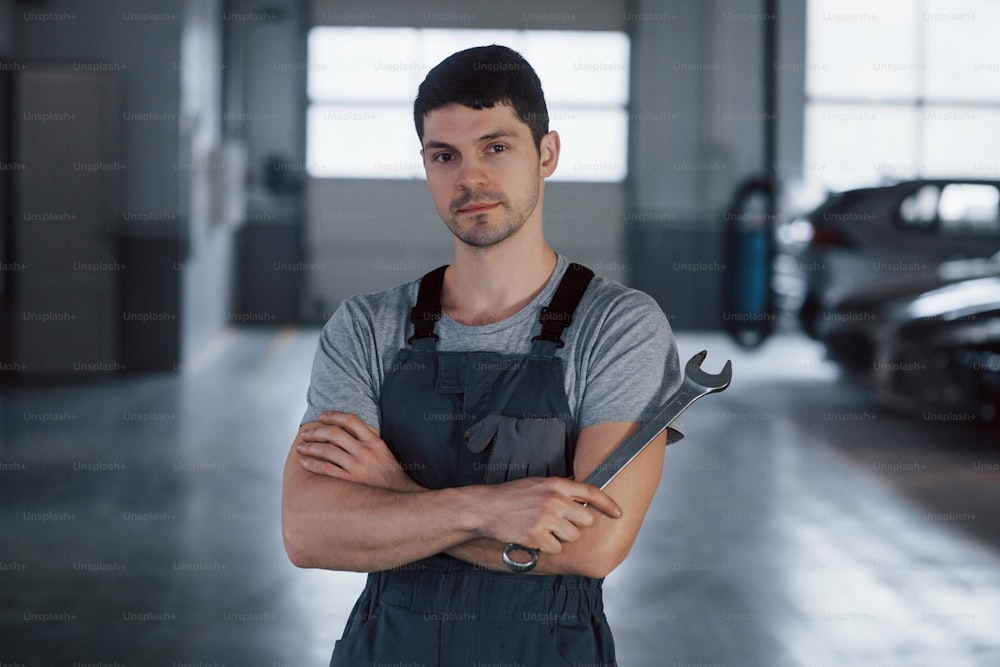 Calm and focused. Portrait of serious worker in uniform that stands in his workshop with wrench in hand.