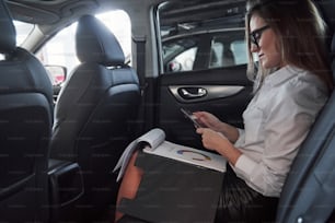 Documentos en el bloc de notas. Una mujer de negocios inteligente se sienta en el asiento trasero del automóvil de lujo con interior negro.