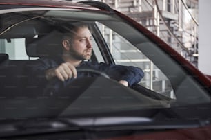 Thoughtful look. Front view of young bearded businessman sitting in his luxury red car.