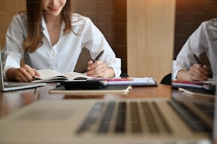 Female writing notebook paper on office desk.