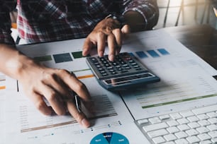 Man working on desk office with using a calculator to calculate the numbers from financial documents, finance accounting concept