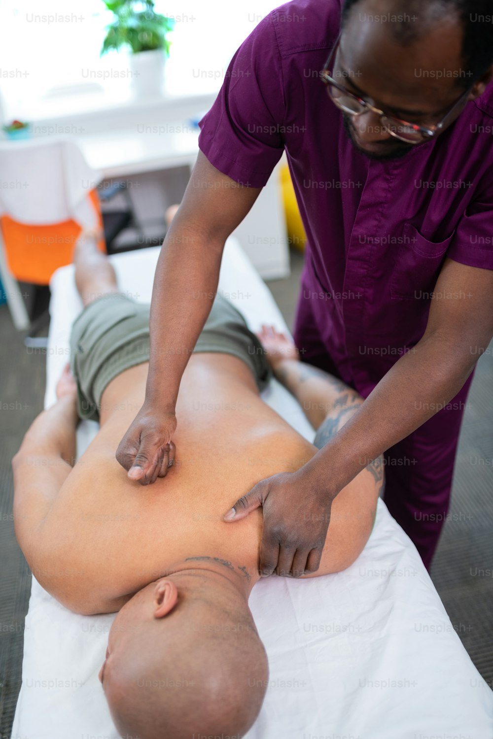 Massaging back. Experienced skillful dark-skinned massage master massaging back for sportsman