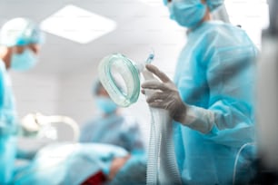 Gros plan d’un bras féminin dans un gant stérile préparant l’�équipement respiratoire pour le patient pendant la chirurgie. Dame portant un masque de protection et une blouse bleue