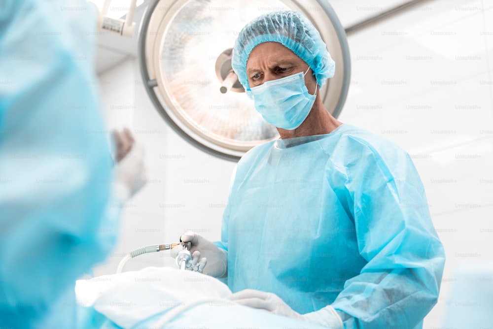 Retrato de cintura para arriba del cirujano con bata azul estéril y gorro usando instrumento laparoscópico durante la operación quirúrgica