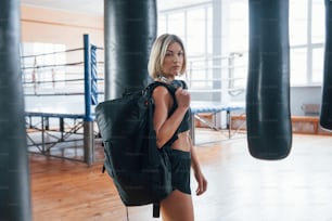 Confident look. Adult female with black bag and headphones in the training gym.
