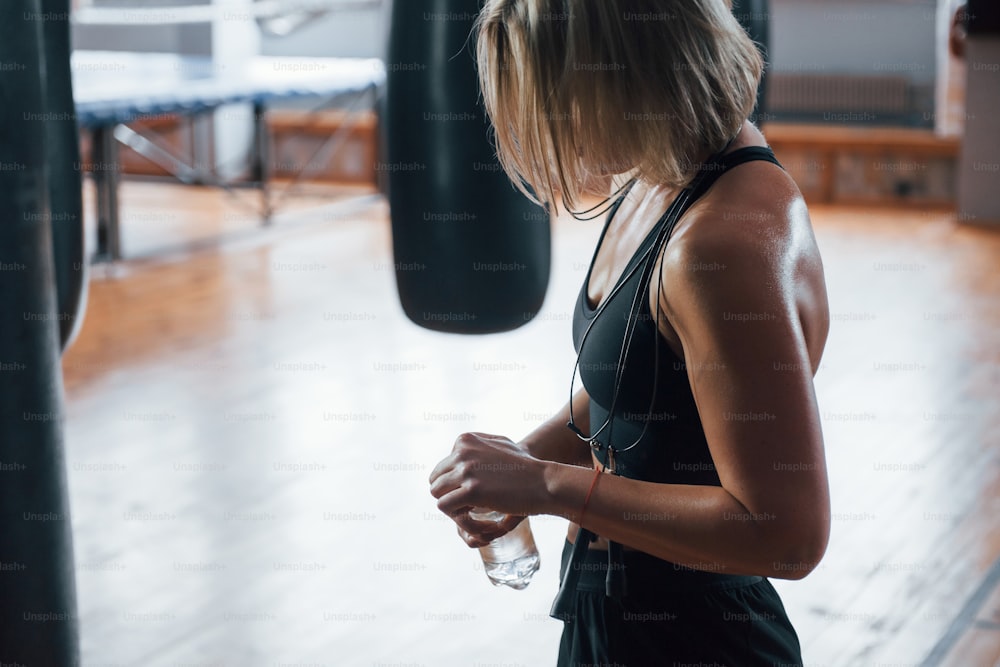 Fresh water needed. Woman near the black punching bag in the gym. Natural lighting.