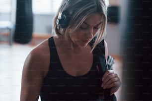 Woman in headphones and in black sports clothes in is the gym.