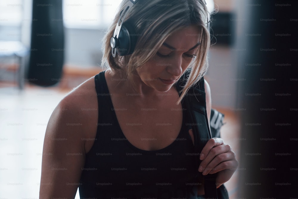 Woman in headphones and in black sports clothes in is the gym.