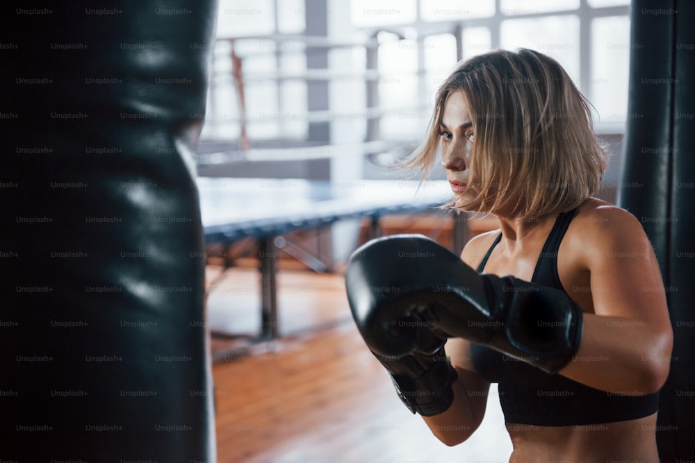 Sweat on the skin. Female boxer is punching the bag. Blonde have exercise in the gym.