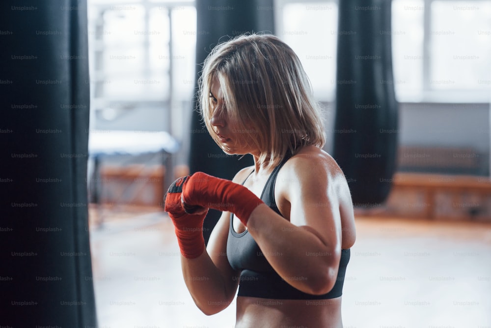 Energy and power. Female boxer is punching the bag. Blonde have exercise in the gym.