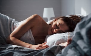 Sunlight do not interfere to sleep. Pretty young woman lying on the bed at morning time in her room.