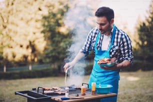 Handsome happy male preparing barbecue outdoors for friends