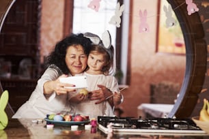 白いスマートフォンで自撮り。祖母と孫娘はイースターの時期に台所で楽しんでいます。