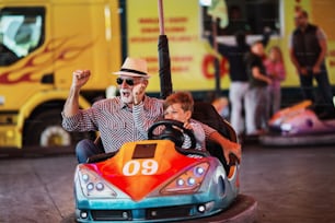 Großvater und Enkel haben Spaß und verbringen eine gute Zeit zusammen im Vergnügungspark. Sie genießen und lächeln, während sie gemeinsam Autoscooter fahren.