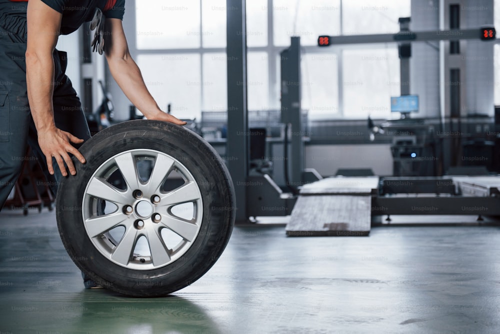 Vue ancrée. Mécanicien tenant un pneu au garage de réparation. Remplacement des pneus d’hiver et d’été.