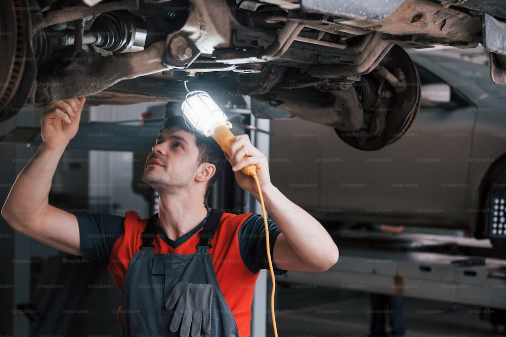 Rusty vehicle. Man at the workshop in uniform fixes broken parts of the car.