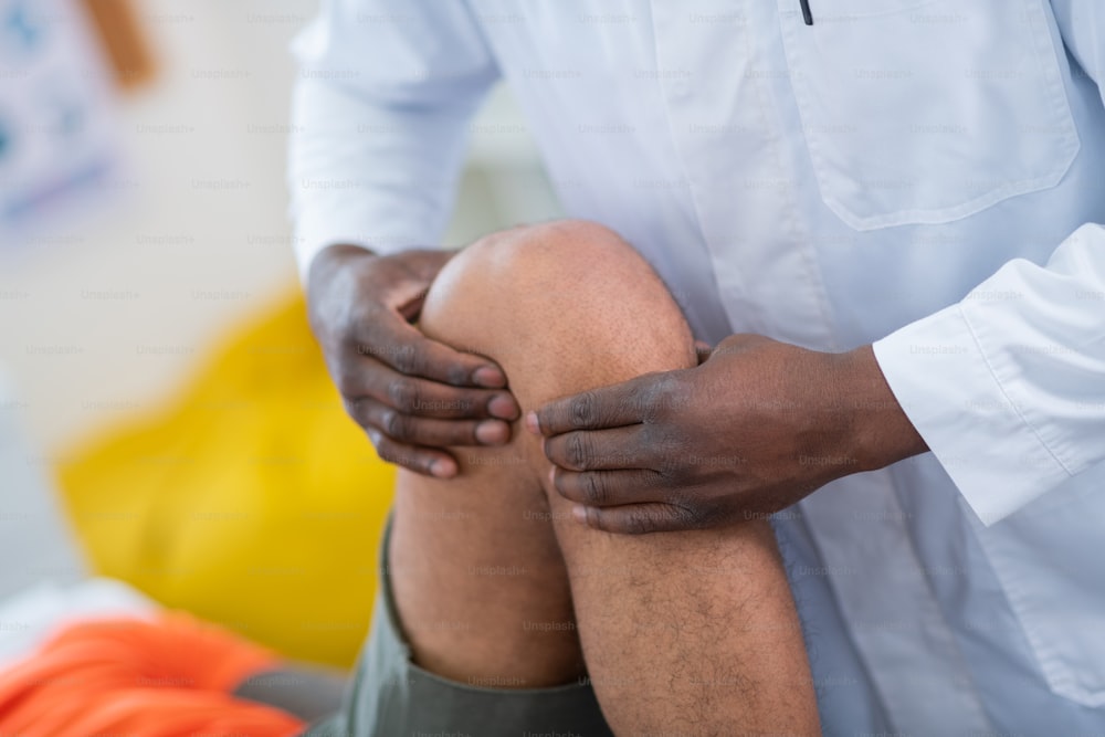 Touching leg. Dark-skinned therapist touching leg and knee of sportsman coming to him