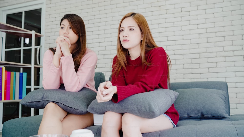 Lesbian Asian couple crying while watching drama in TV in living room at home, sweet couple enjoy romantic moment while lying on the sofa when relax at home. Lifestyle couple relax at home concept.