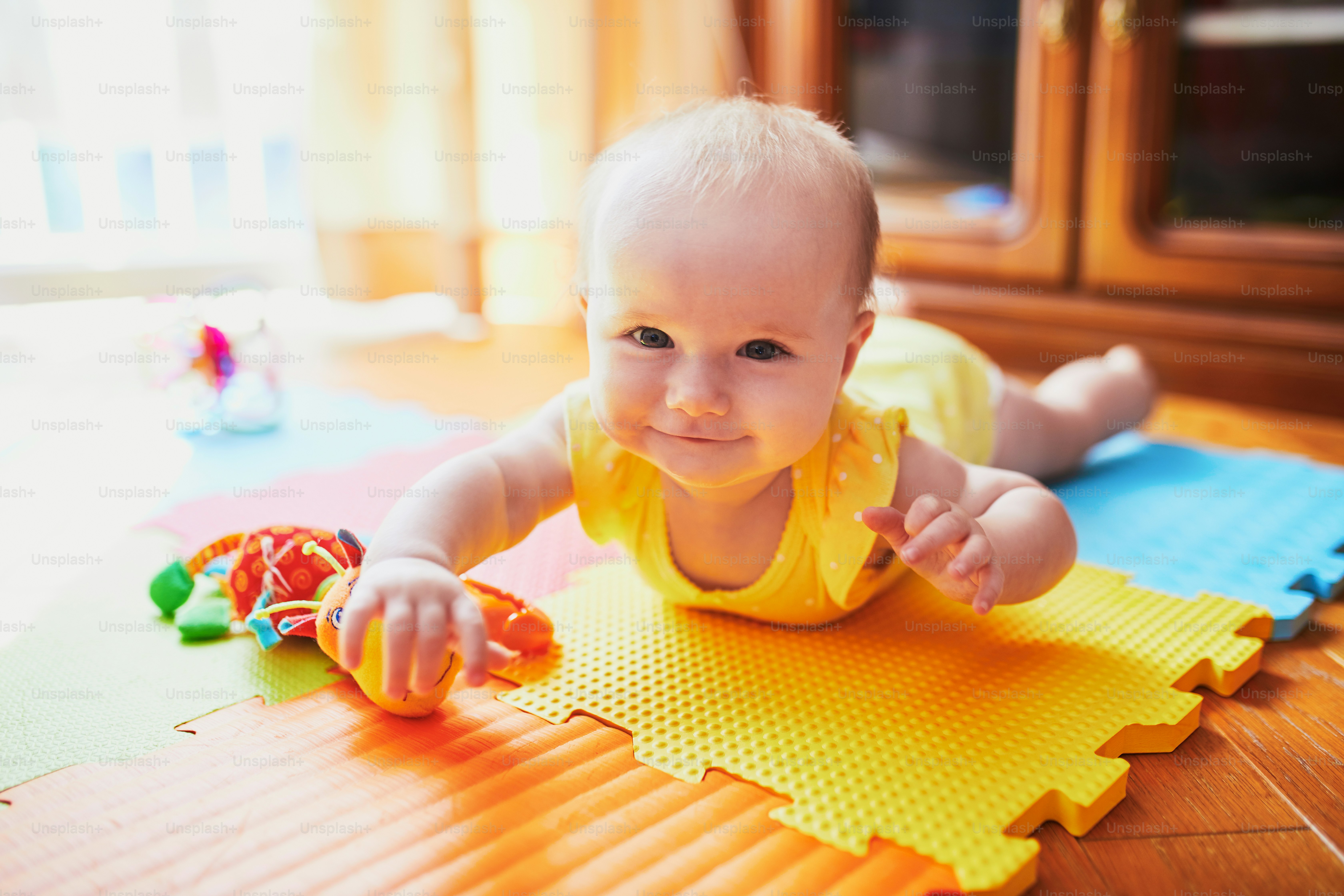 Happy smiling baby girl lying on colorful play mat on the floor photo