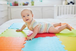 床のカラフルなプレイマットに横たわっている幸せな笑顔の女の赤ちゃん