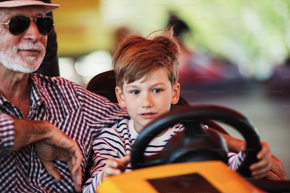 Grandfather and grandson having fun and spending good quality time together in amusement park. They enjoying and smiling while driving bumper car together.