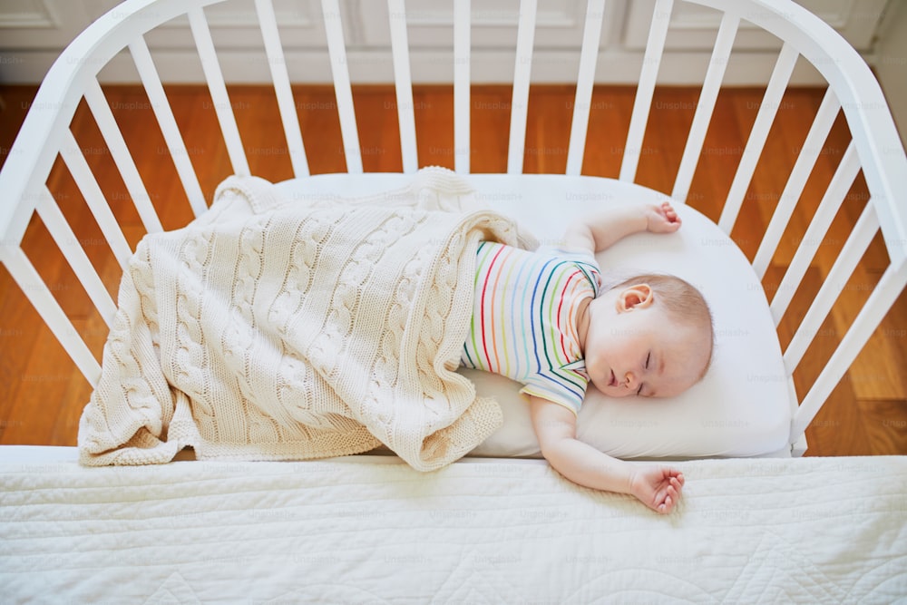 부모의 침대에 부착된 공동 수면 침대에서 자고 있는 사랑스러운 여자 아기. 유아용 침대에서 낮잠을 자는 어린 아이. 수면 훈련 개념입니다. 햇볕이 잘 드는 보육원의 유아 아이