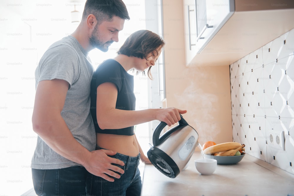 Embracing the girl. Young couple in the modern kitchen at home at their weekend time in the morning.