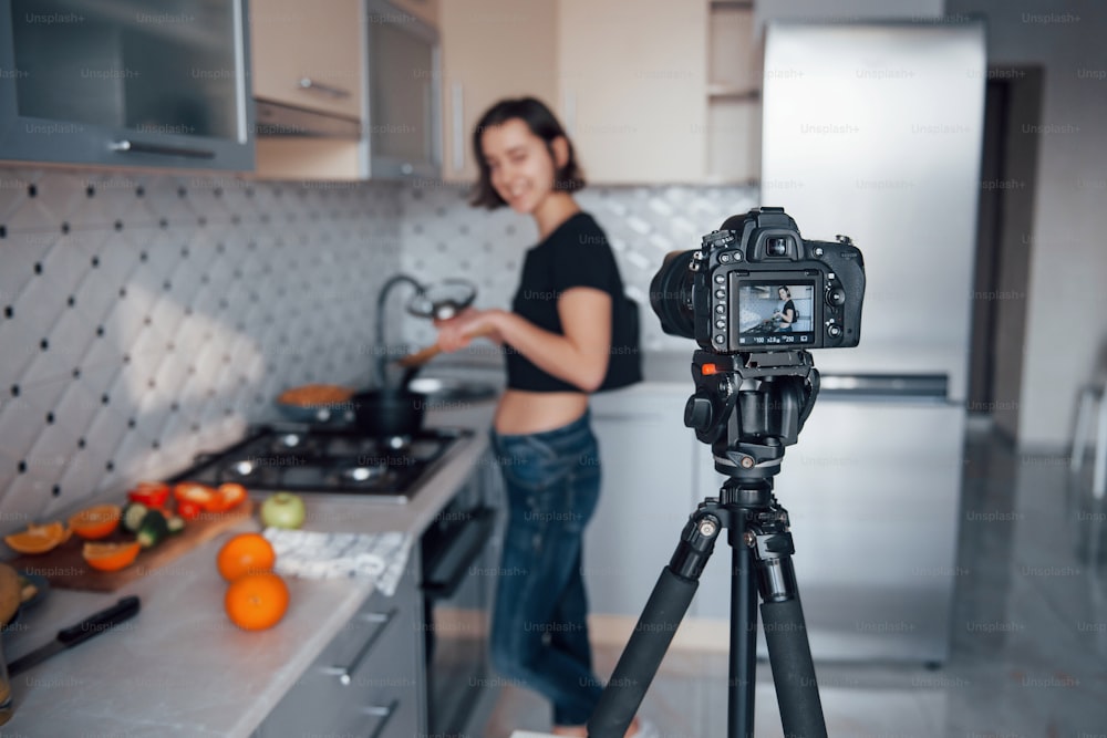 Concentre-se na câmera. Menina na cozinha moderna em casa em seu horário de fim de semana pela manhã.