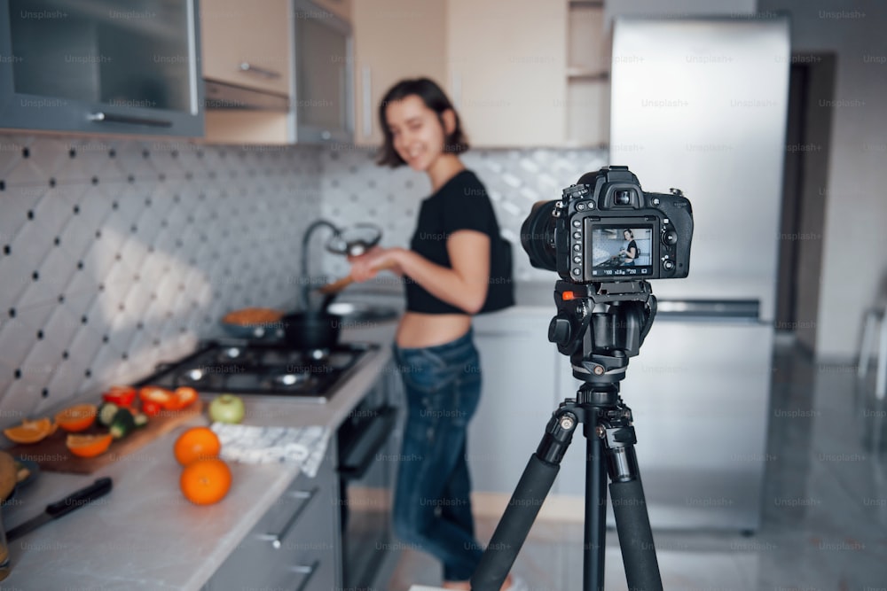 Focus on the camera. Girl in the modern kitchen at home at her weekend time in the morning.