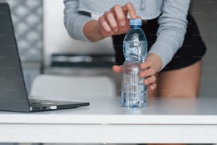 Opening bottle of water. Girl in the modern kitchen at home at her weekend time in the morning.