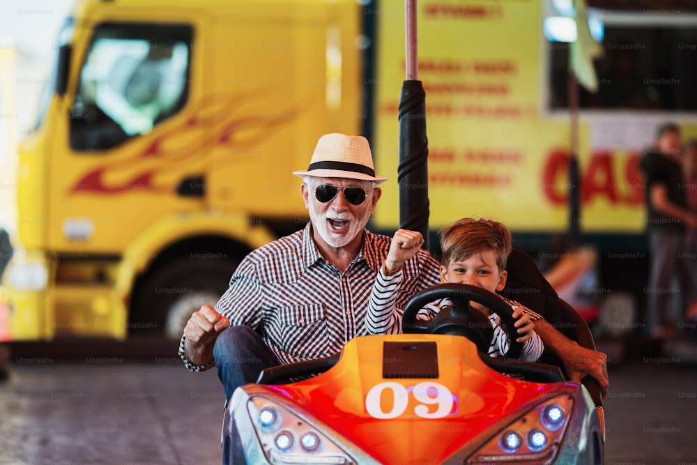 Nonno e nipote che si divertono e trascorrono del tempo di buona qualità insieme nel parco divertimenti. Si divertono e sorridono mentre guidano insieme l'autoscontro.
