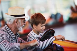 Grandfather and grandson having fun and spending good quality time together in amusement park. They enjoying and smiling while driving bumper car together.