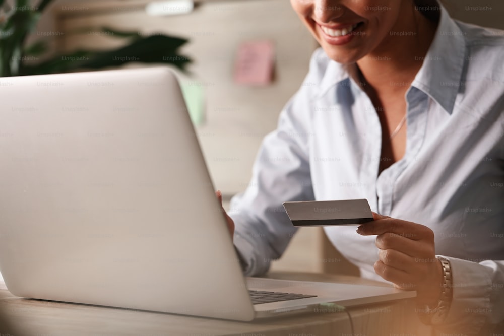 Primer plano de la mujer de negocios que compra en Internet con tarjeta de crédito y computadora portátil en la oficina.