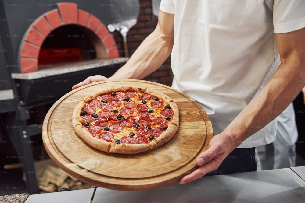 強い男の手。ソーセージリングとオリーブで準備されたおいしいピザの写真。