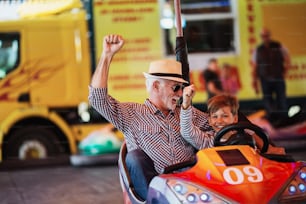 Abuelo y nieto divirtiéndose y pasando tiempo de buena calidad juntos en el parque de atracciones. Disfrutan y sonríen mientras conducen juntos un auto chocador.