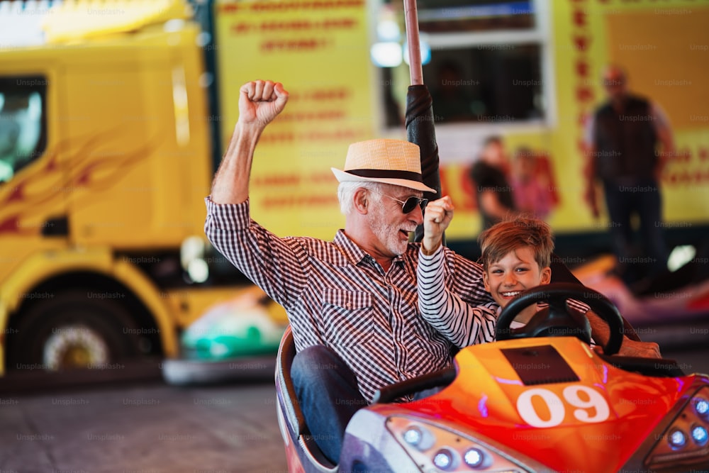 Grandfather and grandson having fun and spending good quality time together in amusement park. They enjoying and smiling while driving bumper car together.