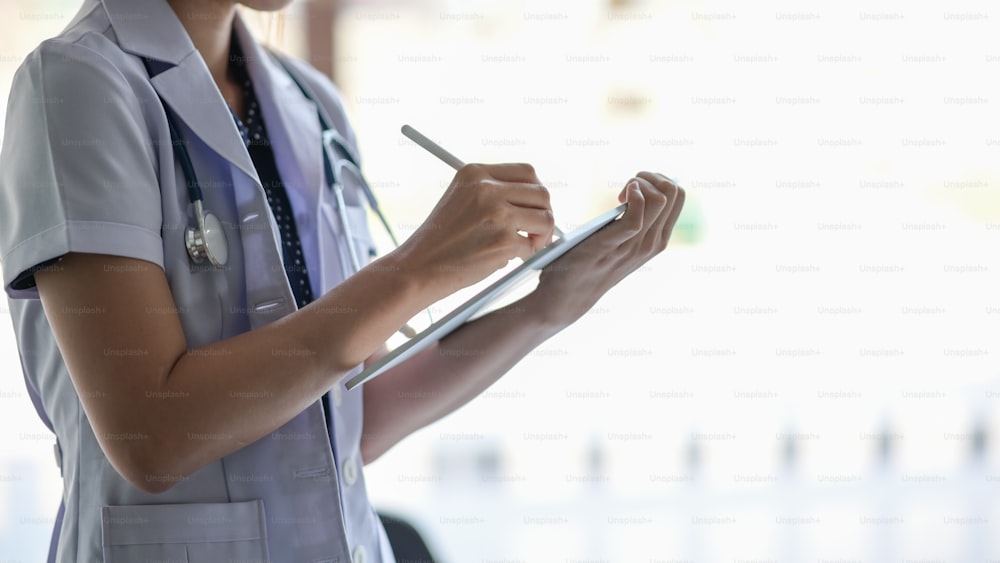 Médico do sexo feminino segurar tablet digital e escrever na tela sensível ao toque no consultório