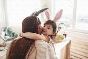 Feeling satisfied. Mother and daughter in bunny ears at easter time have some fun in the kitchen at daytime.