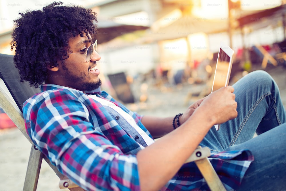 Banking online, portrait of happy african business man with tablet on the beach