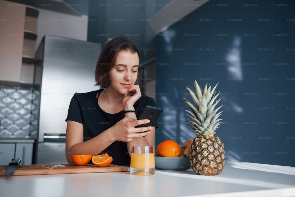 Brunette using phone. Girl in the modern kitchen at home at her weekend in the morning time.